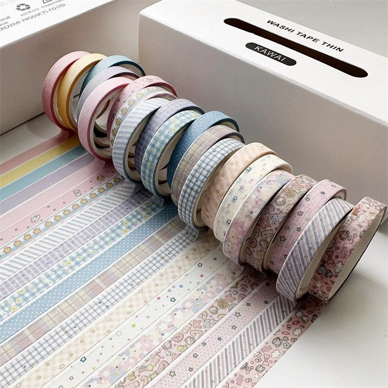 May include: A set of 15 colorful washi tapes with various patterns, including stripes, polka dots, and floral designs. The tapes are arranged in a stack and labeled "Washi Tape Thin Kawaii".