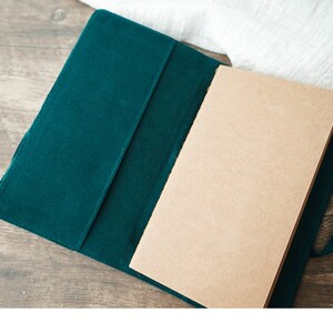 May include: A green corduroy notebook cover with a blank, brown paper notebook inside.