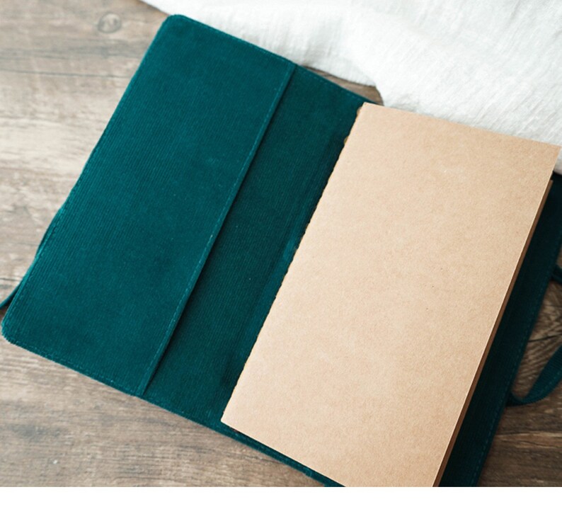 May include: A green corduroy notebook cover with a blank, brown paper notebook inside.