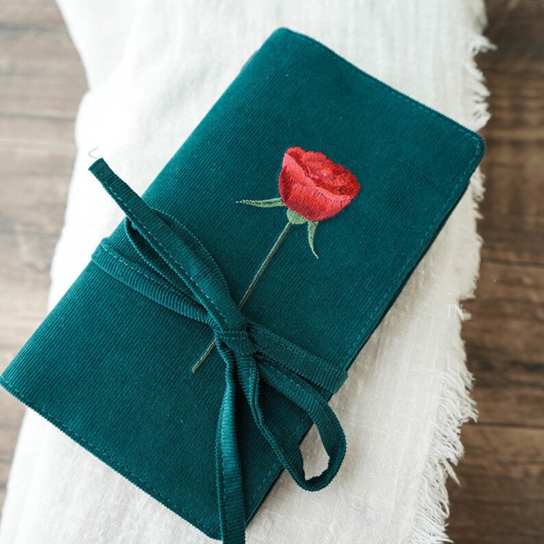 May include: A dark green velvet pouch with a red embroidered rose and a matching green ribbon tie.