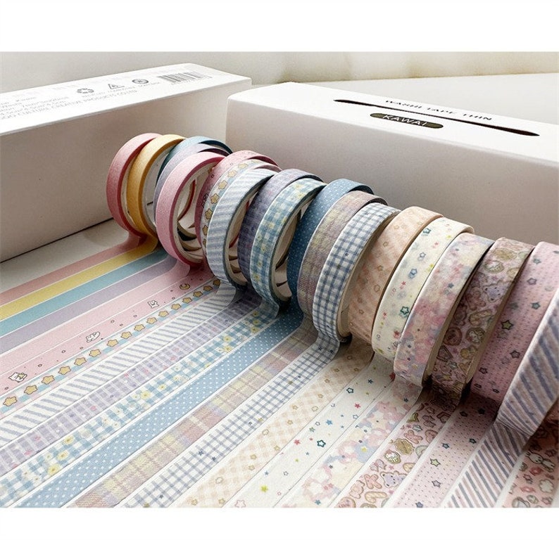 May include: A collection of 15 washi tapes with various patterns, including stripes, polka dots, and floral designs. The tapes are in pastel colors, such as pink, blue, and yellow. The tapes are arranged in a row, with the ends of the tapes overlapping.