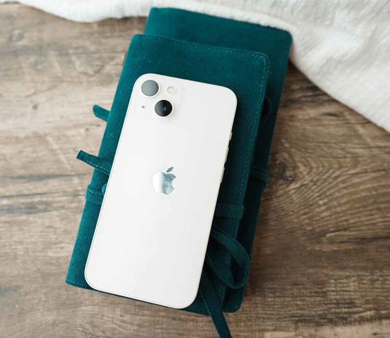 May include: A white iPhone with a green case. The phone has a camera lens with two circles and an Apple logo.