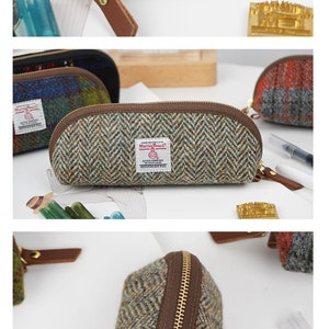 May include: A pencil case made of Harris Tweed wool fabric featuring a brown zipper and a brown leather pull tab. The case has a herringbone pattern in shades of green and gray, with a white rectangular label that reads Harris Tweed.