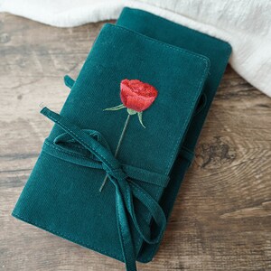 May include: A dark green corduroy journal with a red embroidered rose and a matching green ribbon closure.