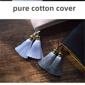 May include: A set of two book covers with embroidered designs. The first cover is made of furry velvet and features a pink flower design. The second cover is made of pure cotton and features a blue and white flower design. The third cover is made of pure cotton and features a crane design. The fourth cover is made of black fabric and features a yellow and black tassel bookmark. The fifth cover is made of blue fabric and features a white flower design.