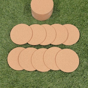 May include: A stack of 12 round cork coasters in a light brown color. The coasters are arranged in a circle on a green grassy surface.