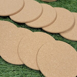 May include: A set of 10 round cork coasters in a natural brown color. The coasters are arranged in a circle on a green artificial grass surface.
