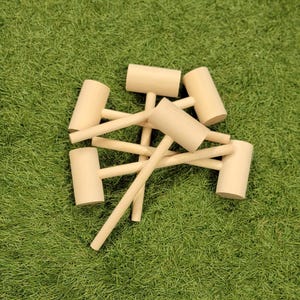 May include: A set of wooden mallets with natural wood handles. The mallets are arranged in a pile on a green artificial grass surface.