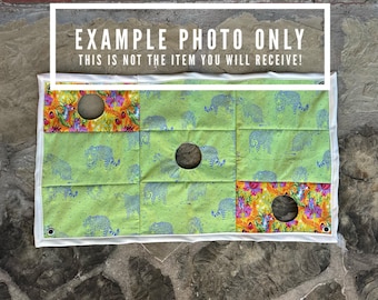 Puede incluir: Un juego de tela con tres aberturas circulares. Tiene un fondo verde con patrones de elefantes azules y diseños florales coloridos en las secciones superior e inferior. El texto "EXAMPLE PHOTO ONLY" está en la parte superior.