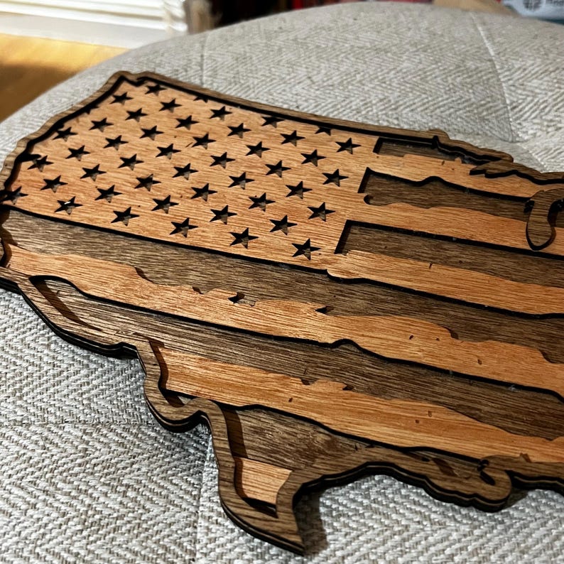 K&ouml;nnte beinhalten: Ein Holzausschnitt der Vereinigten Staaten von Amerika in Form einer Flagge. Die Sterne und Streifen sind aus dem Holz geschnitten, wodurch ein dreidimensionaler Effekt entsteht.