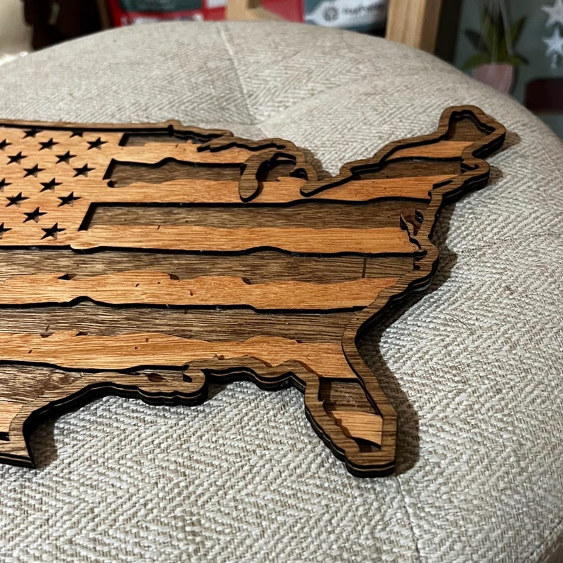 K&ouml;nnte beinhalten: Ein Holzausschnitt der Vereinigten Staaten von Amerika mit dem Design der amerikanischen Flagge. Das Holz ist dunkelbraun mit einer nat&uuml;rlichen Holzmaserung.