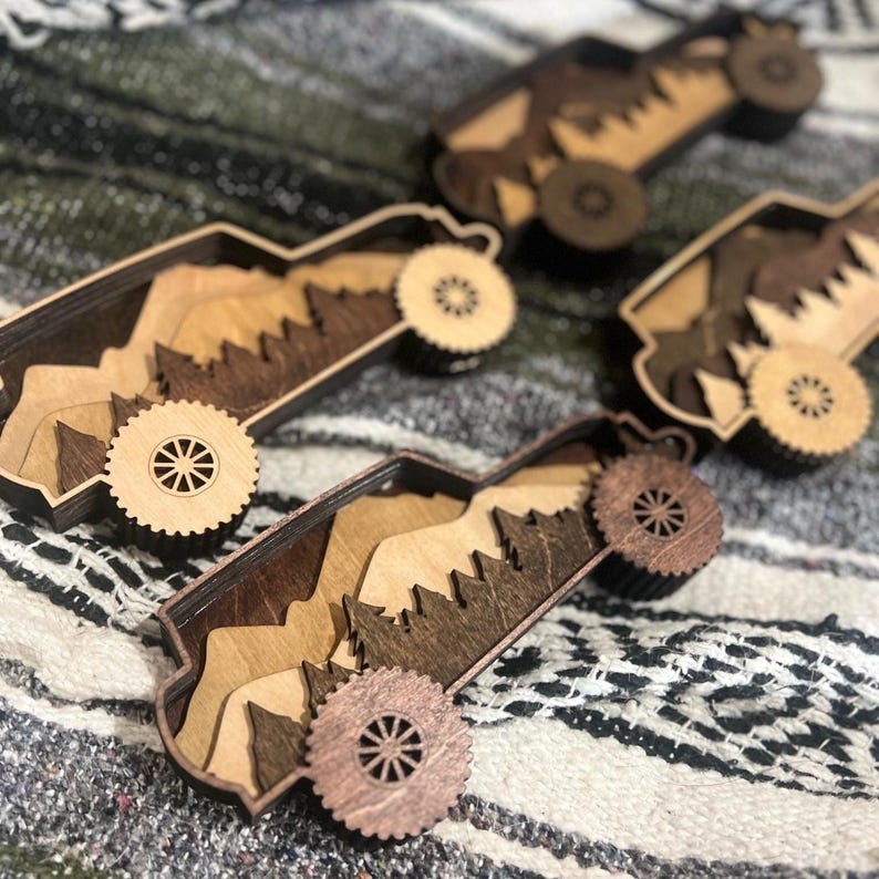 May include: Four wooden toy trucks with mountain and tree cutouts inside. The trucks have wheels and are made of various shades of brown wood. The background is a patterned blanket.