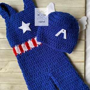 May include: A blue crocheted baby outfit with a red, white, and blue stripe and a white star. The outfit comes with a matching blue crocheted hat with a white letter A.