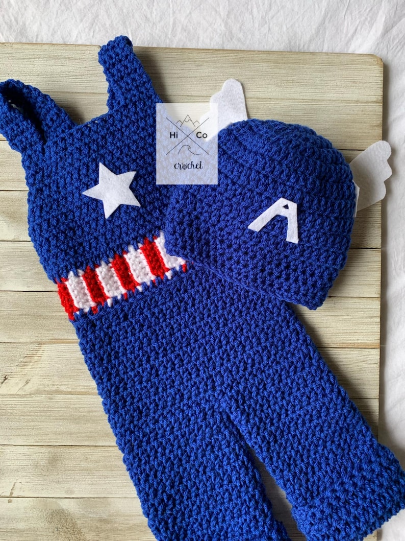 May include: A blue crocheted baby outfit with a red, white, and blue stripe and a white star. The outfit comes with a matching blue crocheted hat with a white letter A.