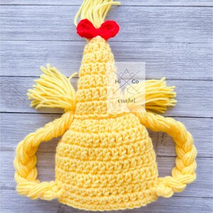 May include: Yellow crocheted hat with a braided ponytail and a red bow. The hat is designed to look like a character with a ponytail.
