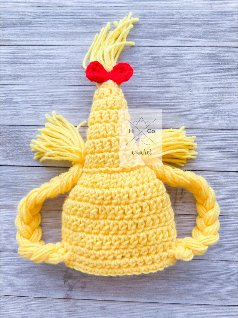 May include: Yellow crocheted hat with a braided ponytail and a red bow. The hat is designed to look like a character with a ponytail.