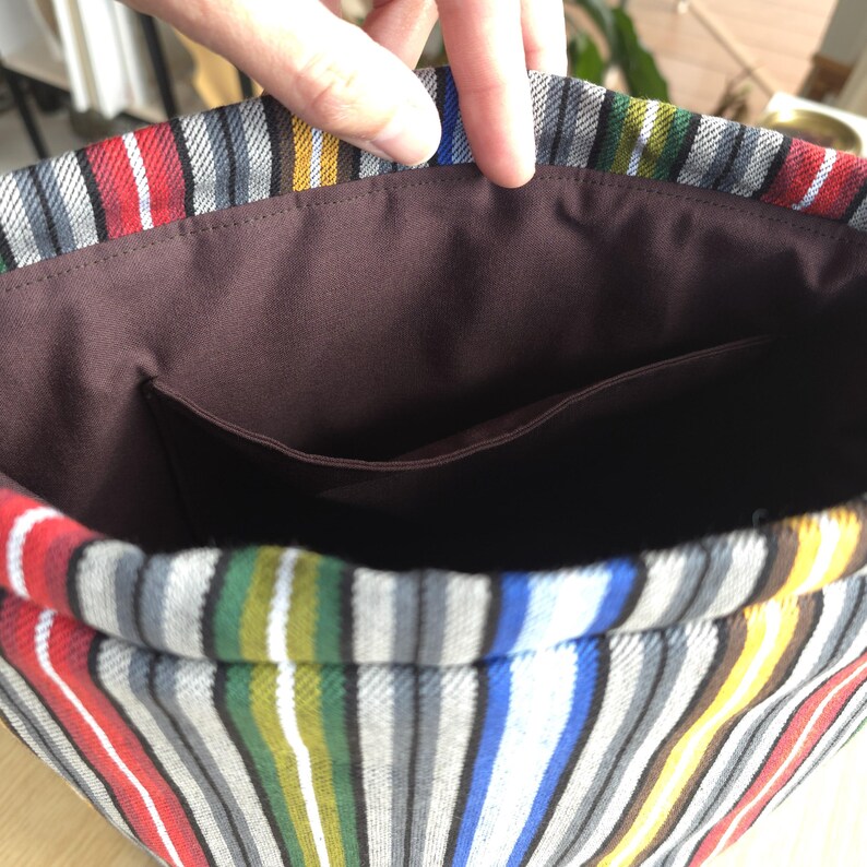 May include: A colorful striped tote bag interior with a brown pocket. The bag's fabric features vertical stripes in red, blue, yellow, green, and gray. The interior is a solid brown color.