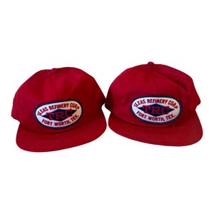 May include: Two red baseball caps with a white oval patch that says "Texas Refinery Corp. TRC Fort Worth, Tex."