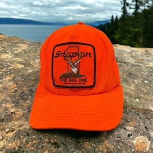 May include: Orange Snap-on brand baseball cap with a black patch featuring a deer and the text "The Big One".