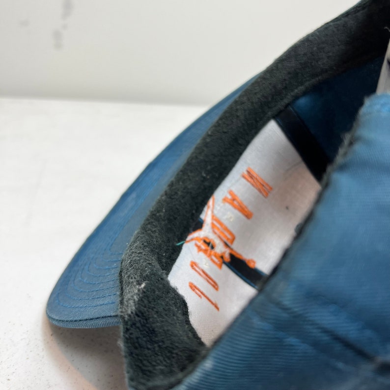 May include: A blue baseball cap with a black brim and a white label with the text "JORDAN" and an orange logo.