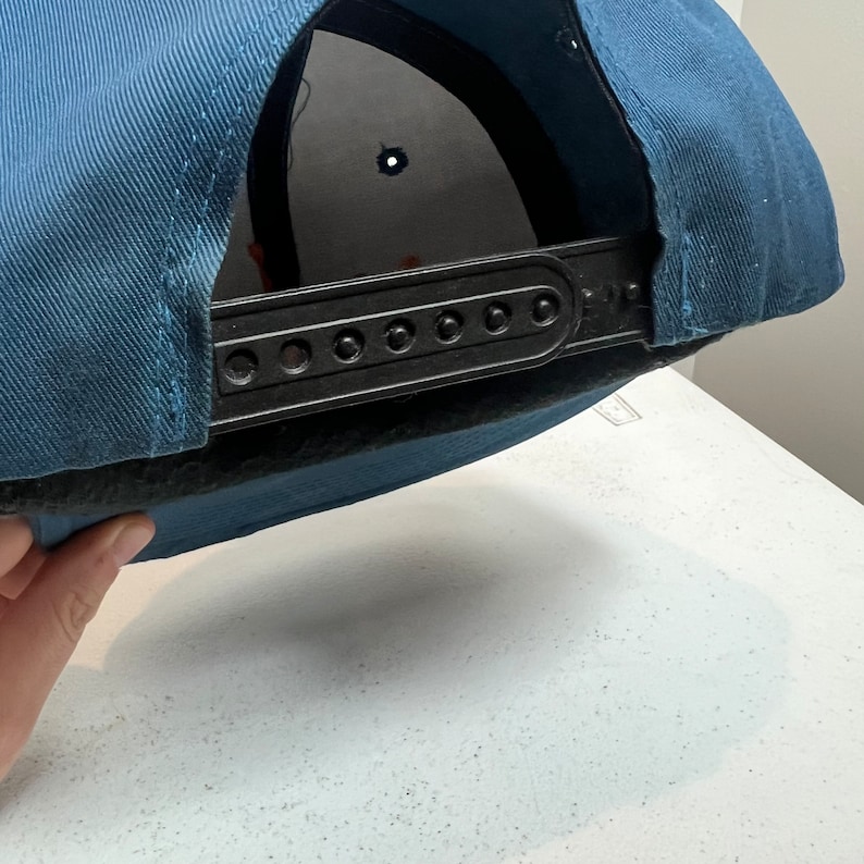 May include: A blue baseball cap with a black adjustable strap and a black mesh lining.