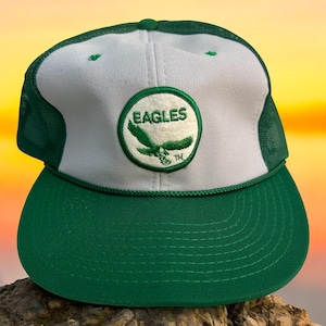 May include: A vintage green and white trucker hat with a green and white embroidered patch that says "EAGLES" with a flying eagle and the trademark symbol.