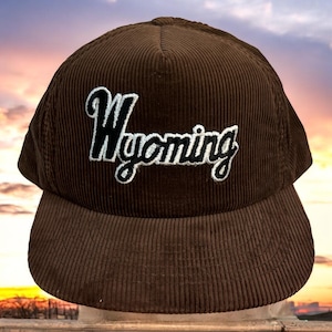 May include: A brown corduroy baseball cap with a black and white embroidered "Wyoming" logo.