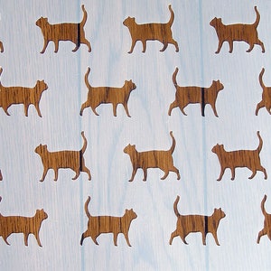 Puede incluir: Una plantilla blanca con 14 siluetas de gatos recortadas. Los gatos están en varias poses, algunos caminando, algunos sentados y algunos acostados. La plantilla es perfecta para crear un diseño con temática de gatos en una variedad de superficies.