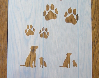 Könnte beinhalten: Eine weiße Schablone mit einem Design aus sieben Pfotenabdrücken und zwei Hunden. Die Pfotenabdrücke sind in verschiedenen Größen und in einem zufälligen Muster angeordnet. Die Hunde sitzen und schauen sich an. Die Schablone befindet sich auf einer Holzoberfläche.