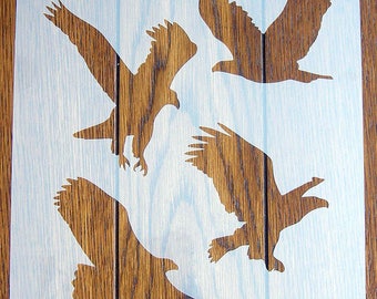 Könnte beinhalten: Eine weiße Schablone mit vier ausgeschnittenen Adler-Silhouetten. Die Schablone befindet sich auf einem Holzgrund.