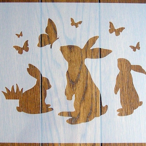 May include: A white stencil featuring three rabbit silhouettes and several butterfly silhouettes. The rabbits are facing different directions. The butterflies are scattered around the rabbits.