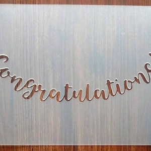 May include: A clear plastic stencil with the word "Congratulations!" cut out in a cursive font.