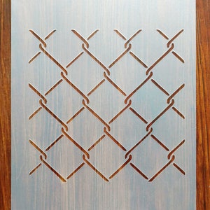 May include: A white plastic stencil featuring a chain link fence design. The stencil is on a wooden surface.