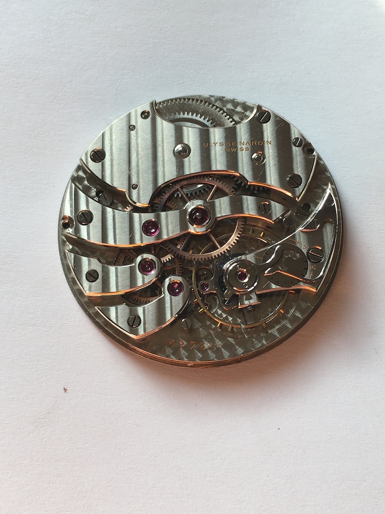 May include: A close-up of a silver watch movement with the text "ULYSSE NARDIN SWISS" printed on the face.