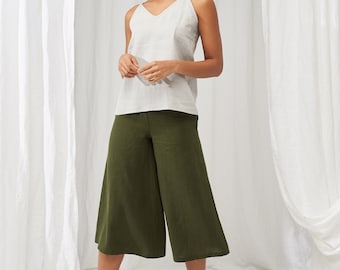 Könnte beinhalten: Eine Person trägt ein hellgraues V-Ausschnitt-Tanktop und olivgrüne Culottes. Das Outfit wird mit beigen Plateausandalen kombiniert. Die Kleidung scheint aus Leinen oder einem ähnlichen Naturstoff zu bestehen, der für warmes Wetter geeignet ist.