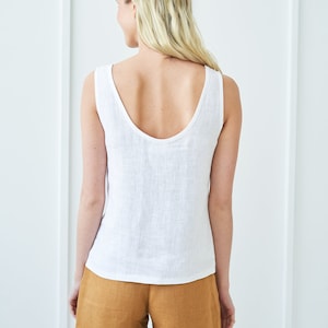 Könnte beinhalten: Ein weißes Tanktop aus Leinen mit einem runden Ausschnitt und einer lockeren Passform. Das Tanktop wird mit braunen Leinenhosen kombiniert.