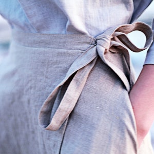 May include: A light gray linen wrap skirt with a self-tie sash. The sash is tied in a bow at the waist.