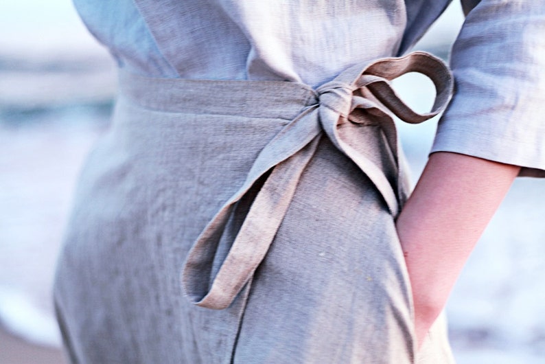 May include: A light gray linen wrap skirt with a self-tie sash. The sash is tied in a bow at the waist.