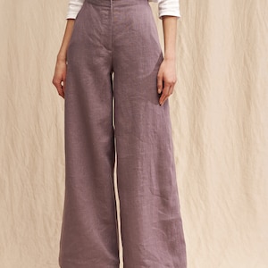 May include: Wide-leg pants in a dusty purple color made from linen. The pants have a high waist and a relaxed fit.