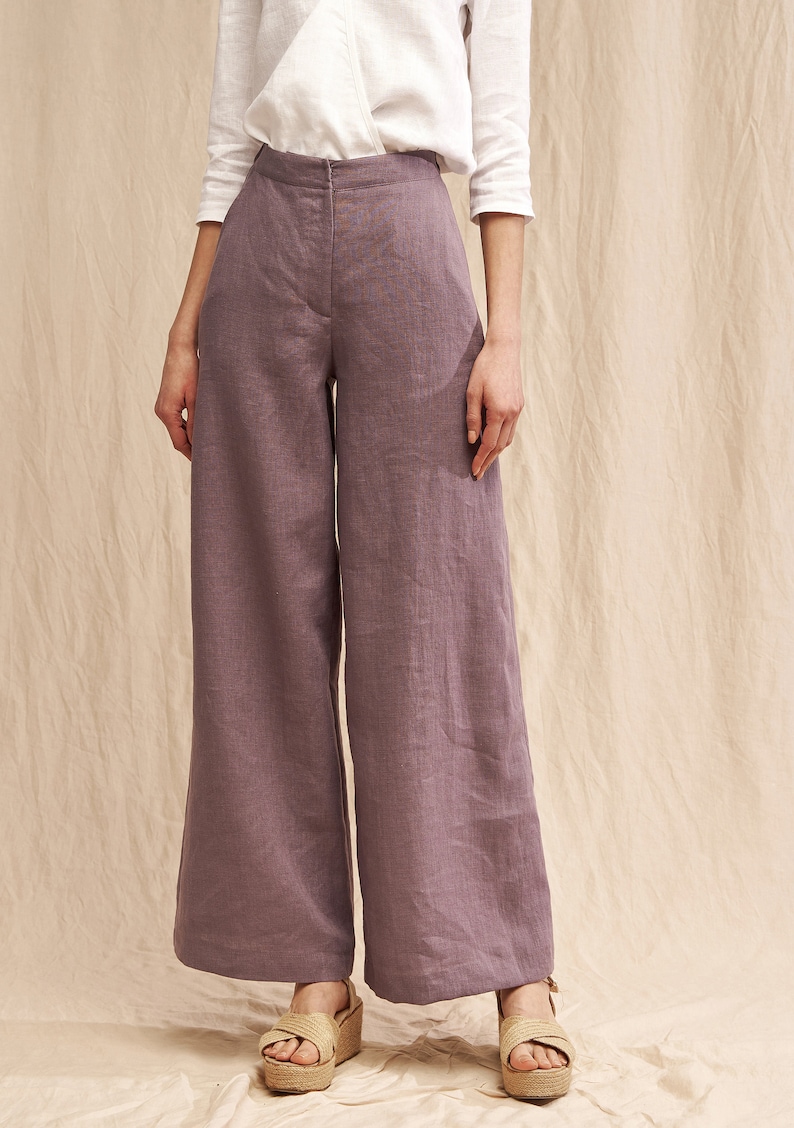 May include: Wide-leg pants in a dusty purple color made from linen. The pants have a high waist and a relaxed fit.