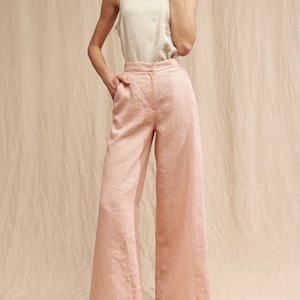 K&ouml;nnte beinhalten: Eine weite Hose in hellrosa. Die Hose ist aus Leinen gefertigt und hat eine hohe Taille. Das Model tr&auml;gt die Hose mit einem wei&szlig;en Tanktop und Plateau-Sandalen.