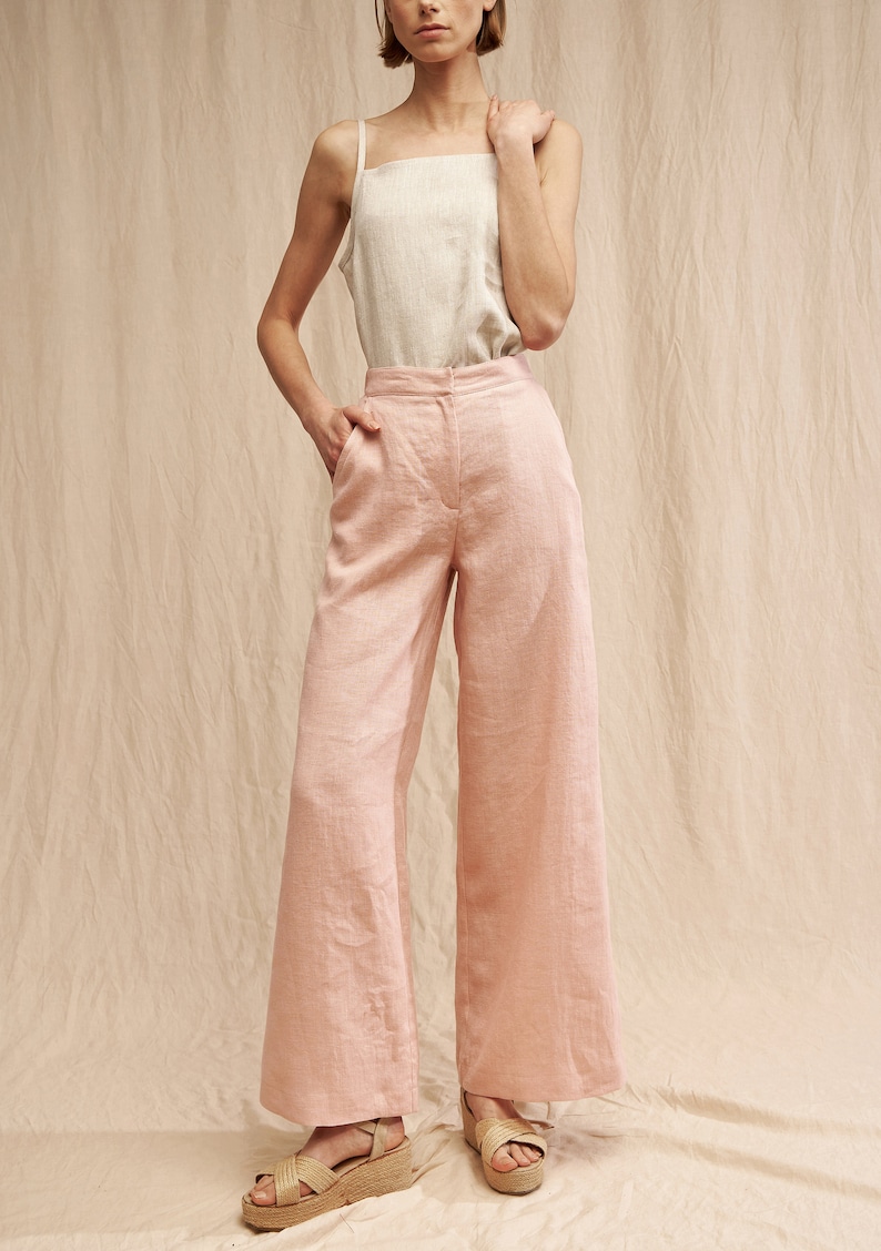 K&ouml;nnte beinhalten: Eine weite Hose in hellrosa. Die Hose ist aus Leinen gefertigt und hat eine hohe Taille. Das Model tr&auml;gt die Hose mit einem wei&szlig;en Tanktop und Plateau-Sandalen.