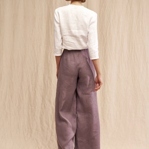 May include: A woman wearing a white linen top and wide-leg linen pants in a dusty purple color. She is wearing platform sandals.