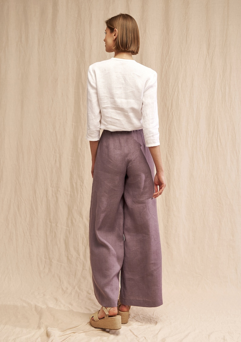 May include: A woman wearing a white linen top and wide-leg linen pants in a dusty purple color. She is wearing platform sandals.