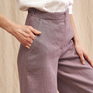 K&ouml;nnte beinhalten: Eine weite Hose in staubigem Lila. Die Hose ist aus Leinen gefertigt und hat eine lockere Passform. Das Model tr&auml;gt ein wei&szlig;es Hemd, das in die Hose gesteckt ist.