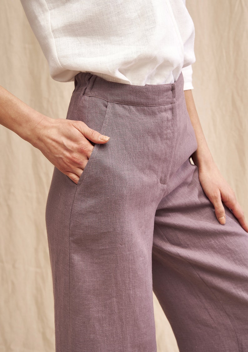 K&ouml;nnte beinhalten: Eine weite Hose in staubigem Lila. Die Hose ist aus Leinen gefertigt und hat eine lockere Passform. Das Model tr&auml;gt ein wei&szlig;es Hemd, das in die Hose gesteckt ist.