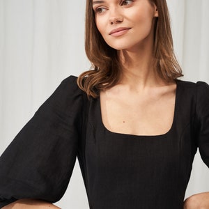 May include: A black linen dress with a square neckline and puffed sleeves. The dress has a fitted bodice and a flowy skirt.