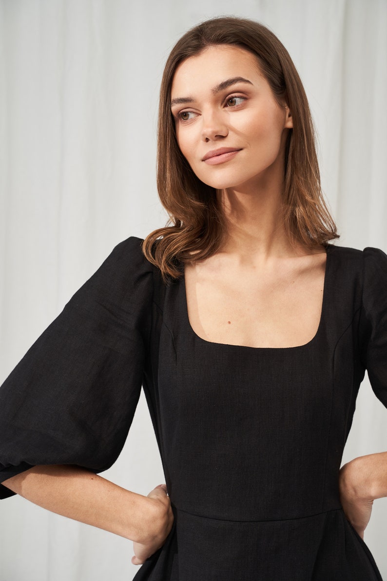 May include: A black linen dress with a square neckline and puffed sleeves. The dress has a fitted bodice and a flowy skirt.