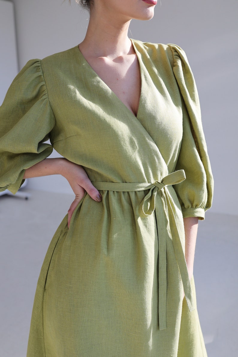 Puede incluir: Un vestido cruzado verde claro con escote en V y mangas cortas abullonadas. El vestido presenta un cintur&oacute;n de tela a juego atado a la cintura. El vestido est&aacute; hecho de una tela texturizada.