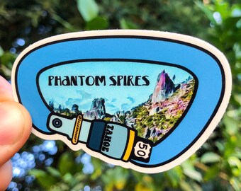 May include: A blue and white sticker featuring a picture of a mountain range with the text "PHANTOM SPIRES" and "TAHOE 50". The sticker is shaped like a climbing carabiner.